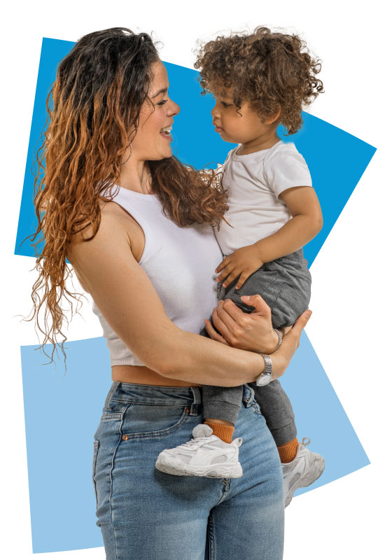 A smiling woman with long, wavy hair holds a young child in her arms. Both are wearing white tops and jeans, standing in front of a white background with blue geometric shapes.