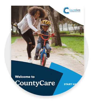 A smiling woman helps a young boy ride a bicycle in a park. The image includes the CountyCare logo and the text “Welcome to CountyCare” and “Start Here.”.